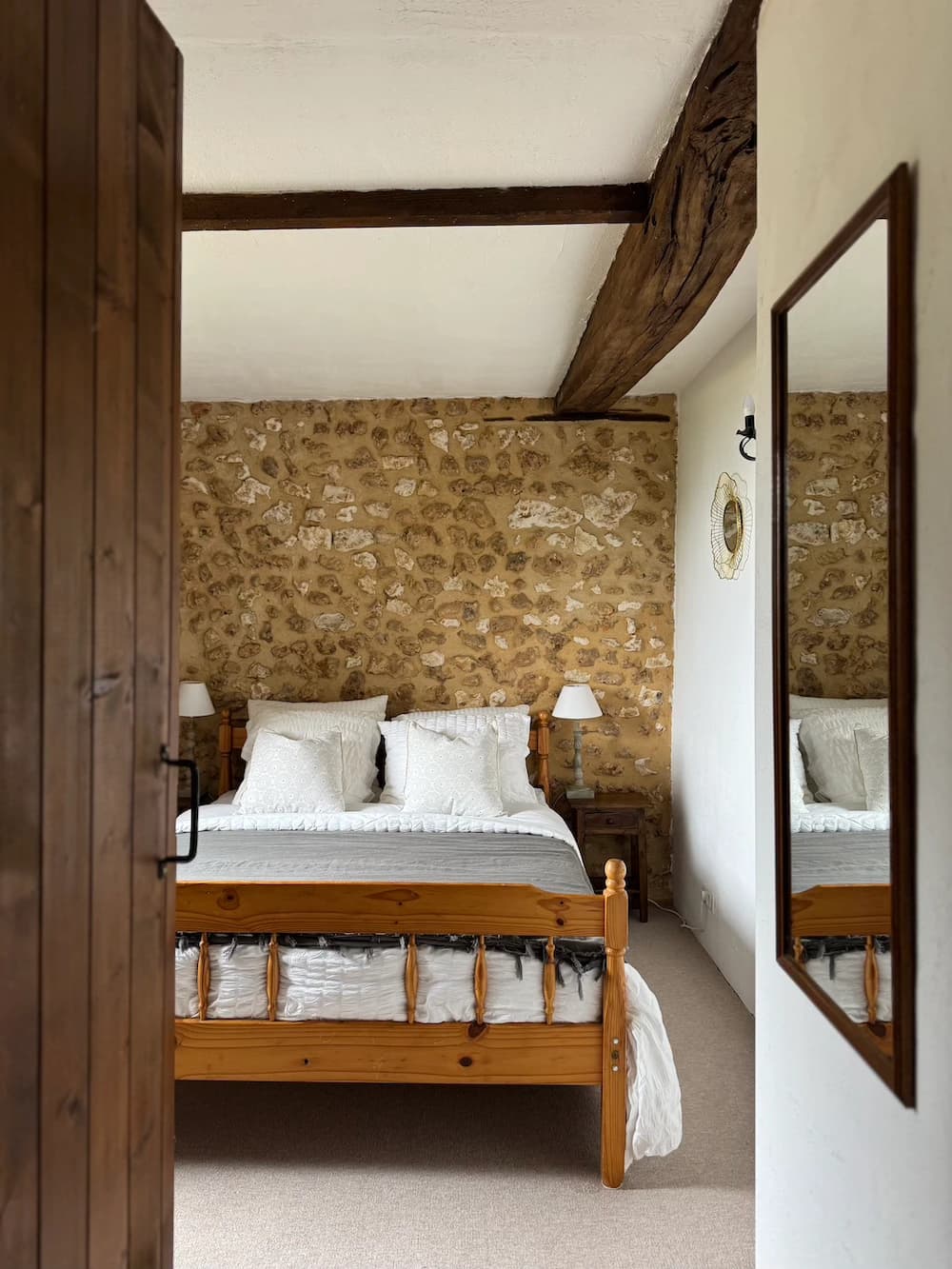 Chambre au mur de pierre, lit en bois et mirroir ovale