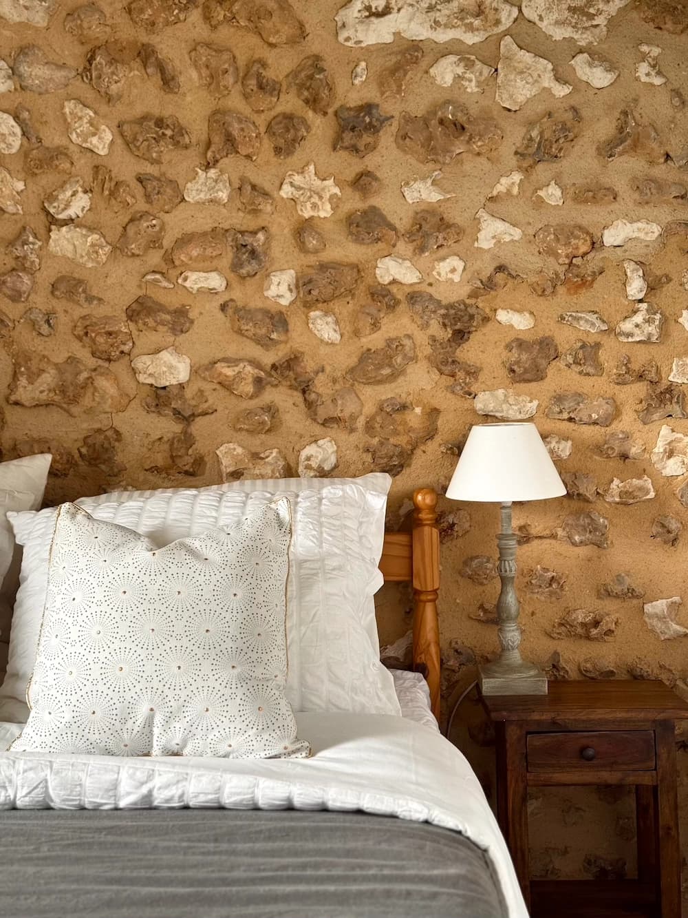 Coussin brodé sur lit blanc, lampe en céramique