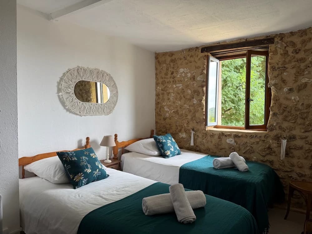 Deux lits jumeaux contre la pierre, fenêtre sur l'arbre