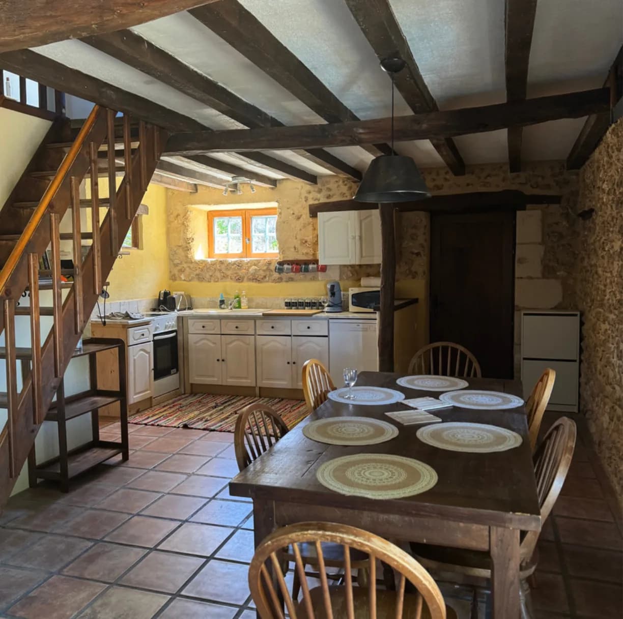 La salle à manger commune, longue table de bois, poutres apparentes et mur de pierre